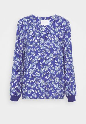 Blå bluse med lange ærmer med hvidt og lyseblåt blomsterprint, rund halsudskæring og ribstrikkede manchetter, vist på en hvid baggrund.