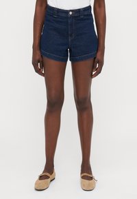 Mørkeblå denimshorts med høy midje, rullede ermer og kontrastsøm. Kombinert med beige leiligheter med stroppdetaljer.
