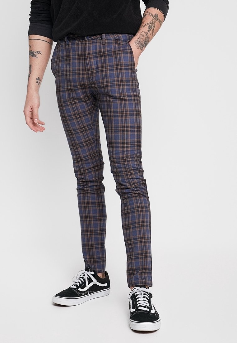 Smal passform rutiga byxor i marinblått med bruna och beige detaljer, med en mjuk tygtextur och minimalistiska designdetaljer.