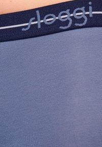 Sloggi-underkläder i lätt blått med ett mjukt, slätt tyg, som har ett marinblått elastiskt midjeband med vita accentstrimmor och logotyp.