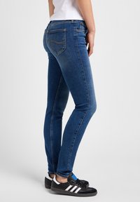 Smal blå jeans med en bleknad textur, kontrasterande sömmar och två bakfickor; i kombination med svarta sneakers med vita ränder.