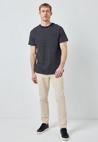 Námořnické pruhované tričko s krátkým rukávem, spárované s krémovými kalhotami a černými teniskami. Jednoduchý, ležérní střih s kulatým výstřihem.