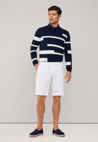 Jersey de marina con rayas horizontales blancas, combinado con pantalones cortos blancos. El modelo lleva zapatillas de slip-on en color marino; textura suave, ajuste casual.