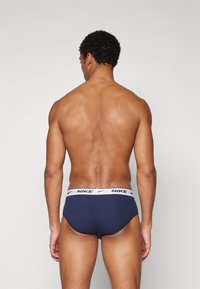 Moške spodnjice temno modre barve z belim elastičnim pasom, na katerem je logotip Nike. Material je videti gladek in tesno prilegajoč.