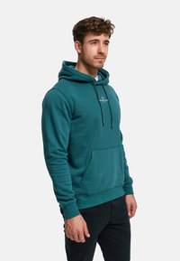 Sudadera con capucha color verde azulado hecha de tela suave, con un bolsillo canguro frontal, capucha con cordón y detalle del logo en el pecho.