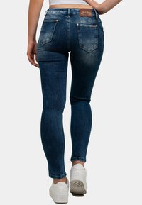 Jeans skinny blu scuro in denim, con vita piatta, due tasche posteriori e una leggera scoloritura. Abbinati a sneakers bianche.