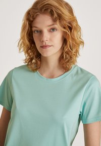 Licht turquoise t-shirt met ronde hals en korte mouwen, gemaakt van gladde stof; heeft een eenvoudig, ongecompliceerd ontwerp.