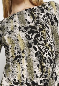 Langärmeliges Oberteil mit figurbetontem Design, das ein abstraktes Muster in Schwarz, Creme und Olivgrün auf einem weichen, dehnbaren Stoff zeigt.