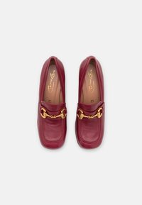 Par af bordeaux læder loafers med guld hestesko detaljer, firkantet tå og beige indlægssåler, set ovenfra på en hvid baggrund.