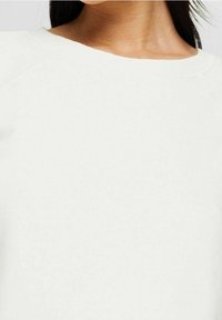Lichtbeige trui, van zacht katoenmateriaal, ronde halslijn met raglanmouwen, gladde textuur, minimale stikseldetails.