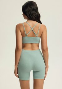 Jasnozielony sportowy zestaw z prążkowanym wzorem, składający się z cropped topu z krzyżującymi się ramiączkami oraz szortów z wysokim stanem, oba z gładkiej tkaniny.