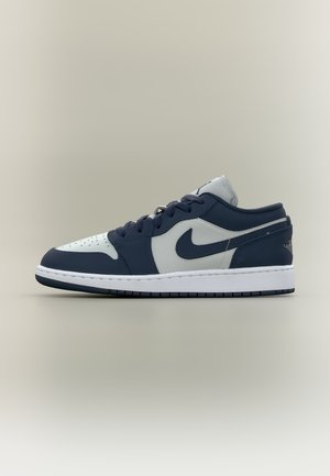Pantof sport Nike low-top din piele bleumarin și alb cu șireturi și talpă albă pe un fundal bej simplu.
