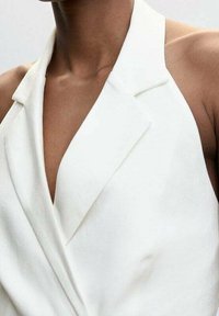 Top blanco de cuello halter con un escote en V profundo, que presenta un diseño estructurado, una textura de tela suave y paneles frontales superpuestos.