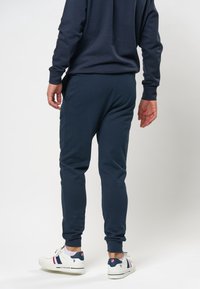 Marine joggers met een gladde textuur, elastische tailleband en taps toelopende benen. Gecombineerd met witte sneakers met blauwe en rode accenten.