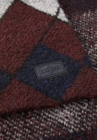 Wollen deken met een diamanten patroon in kastanjebruin, marineblauw en grijs. Een zwart label met "PIER ONE" is in de hoek gestikt.