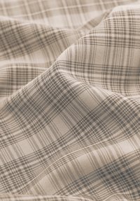 Tissu beige doux avec un motif à carreaux marron clair et foncé, présentant des plis délicats et des détails de texture.