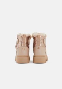 Ružové zlaté členkové topánky s lesklým, polstrovaným zvrškom, umelým kožušinovým podšívaním a hnedou gumovou podrážkou. Obsahujú zadný pútko na obúvanie a zaoblený detail s logom.