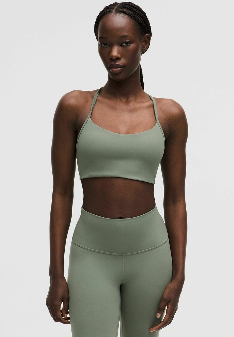 Haut court de sport vert olive à fines bretelles, associé à un legging taille haute. Tissu lisse et extensible avec une coupe ajustée.