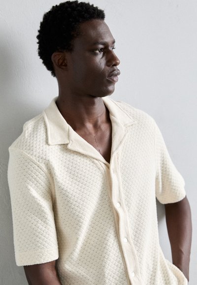 Korte mouwen, crème gebreide polo met een textuurpatroon, kraag en knopen aan de voorkant, met een casual ontwerp.