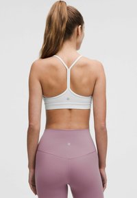 Bílá sportovní podprsenka s tenkými ramínky a designem racerback, spojená s vysokými levandulovými legínami s hladkou texturou.