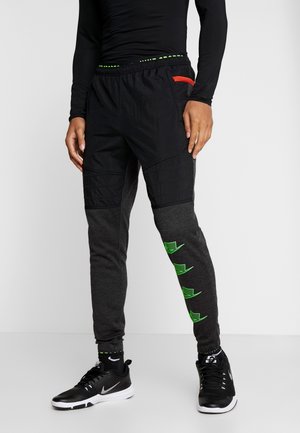 Sorte atletikbukser med en tekstureret øvre del, grå nederste sektion, neongrønne accenter og en orange lomme detalje. Båret med sorte sneakers.