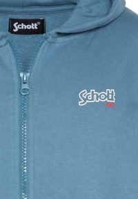 Blauwe hoodie met ritssluiting, gemaakt van zacht materiaal, voorzien van een capuchon, een ritssluiting aan de voorkant en een logo "Schott NYC" in wit en rood aan de linkerkant.