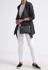 Sac bandoulière noir texturé avec ferrures argentées, associé à un haut léger à pois, une veste noire et un pantalon blanc slim.