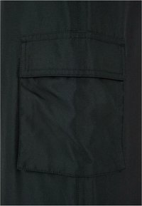 Poche carrée en tissu foncé avec fermeture à rabat cousue sur un fond en matière sombre assortie.