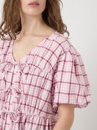 Abito rosa a quadretti con maniche corte a sbuffo, scollatura a V, vita con cordoncino e tessuto testurizzato. Il motivo presenta dimensioni di quadretti alternate.