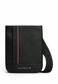 Bolso cruzado de cuero negro con superficie texturizada, que presenta un acento a rayas y un logo en la parte inferior. Correa de nylon ajustable.