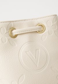 Cream-colored bucket bag made of textured synthetic leather featuring embossed floral patterns and gold-colored metal hardware.