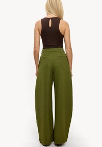 Pantalon vert à jambes larges avec une finition texturée. Conception taille haute avec poches arrière et détail bouton à la ceinture.