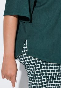 Teal texturovaný top s bočními rozparky spárovaný se vzorovanými zelenými a bílými kalhotami s vysokým pasem, které mají mřížkový design.