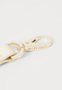 Ivory lærrem med en gulltone metallklips som har gravert "VALENTINO"-logo; glatt tekstur og polert finish.
