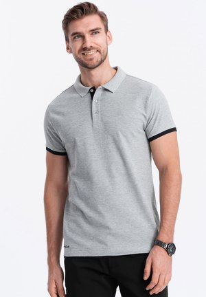 Polo gris con cuello negro y acentos en las mangas, con tapeta de tres botones, hecho de una tela suave. El modelo posa con un reloj en la muñeca izquierda.
