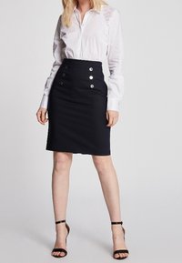 Black skirt with a fitted shape, high waist, and three silver button accents. Paired with a white long-sleeve shirt for contrast.