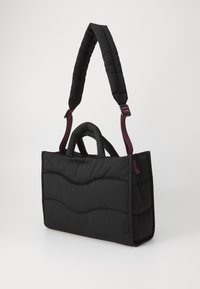 Svart polstret totebag med bølgemønstrede søm, med et topphåndtak og et langt justerbart belte i en kontrastfarge.