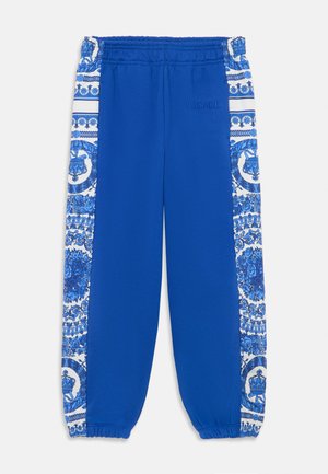 Mėlynos treniruočių kelnės su elastinga juosta, siaurinančiais rankogaliais ir dekoratyvinėmis baltomis šoninėmis juostelėmis su sudėtingais mėlynais raštais. Išsiuvinėtas Versace logotipas.