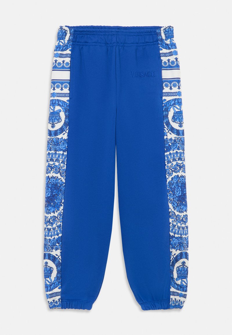 Calças de treino azuis com faixa elástica na cintura, punhos ajustados e painéis laterais brancos decorativos com padrões intrincados em azul. Logótipo da Versace bordado.