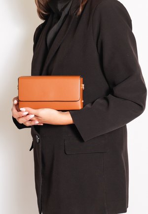 Tan rechthoekige clutch van glad leer, met een zwarte rand. De tas heeft een klepsluiting en gouden hardwareaccenten.
