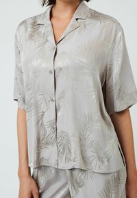 Lys grå natshirt i silkeagtigt stof, der har et palmebladsmønster i sølv, korte ærmer og knaplukning foran.