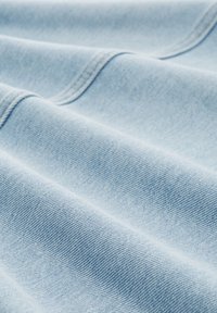 Ljusblå denimtyg med en mjuk textur, med diagonala vävmönster och synliga sömmar längs kanterna.