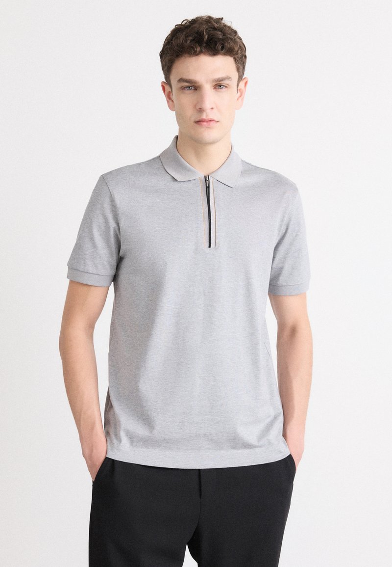 Šedá polokošeľa s krátkymi rukávmi a zipsom pri golieri. Vyrobená z hladkej textílie, m�á jednoliatu farbu a minimalistický dizajn.