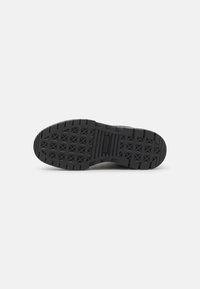 Suela de zapatilla de goma negra con un patrón texturizado y una banda de rodadura en forma de estrella para agarre. Presenta un detalle de logo central.