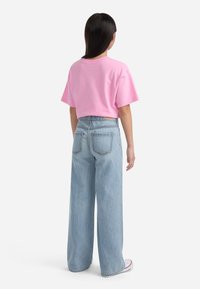 Tricou din bumbac roz, cu mâneci scurte, asortat cu blugi albastri, cu talie înaltă și Croială largă. Ținuta are un fit lejer și un stil casual.