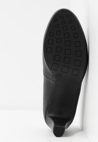 Chaussure en cuir noir avec une texture lisse, bout arrondi et semelle extérieure en caoutchouc flexible dotée d'une traction à motifs carrés. Taille 37 visible.