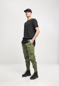 Camiseta negra de manga corta, pantalones cargo verdes oliva con bolsillos laterales y zapatillas negras de caña alta. Diseño simple, ajuste casual.