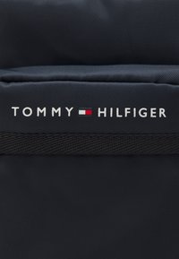 Svart nylonryggsäck med en texturerad yta och en framträdande vit "TOMMY HILFIGER" logotyp med en tri-färgad accent i rött, vitt och blått.