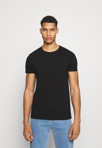 Svart kortermet t-skjorte i en tettsittende design, laget av bomullsstoff, med en klassisk rund hals og rett fald. Bært med lyseblå jeans.
