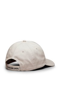 Gorra de béisbol beige hecha de algodón. Presenta un visera curvada, una correa ajustable en la parte posterior y una etiqueta negra de "Calvin Klein Jeans".